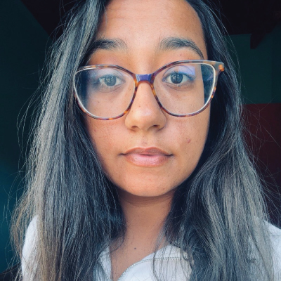 Close-up portrait of a young woman with long dark hair and brown tortoiseshell glasses looking at the camera with a neutral expression.